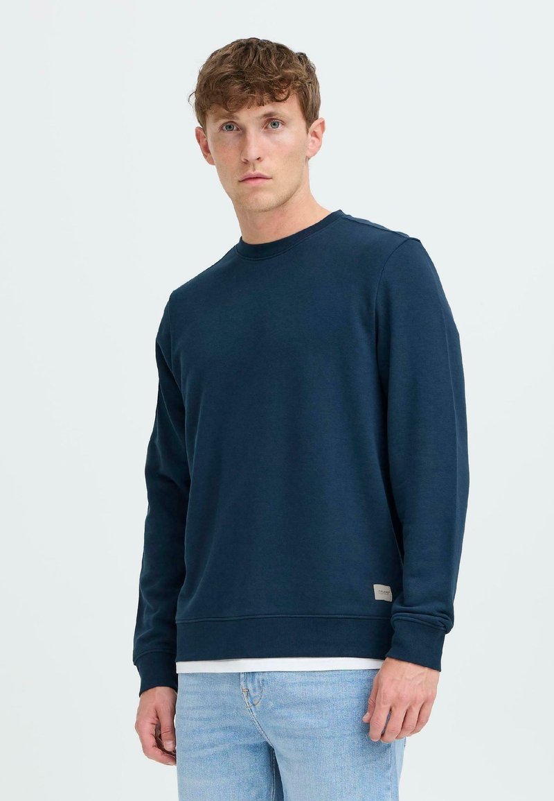 Sudadera navy en mezcla de algodón con mangas largas, cuello redondo, puños y dobladillo de canalé, con una pequeña etiqueta de marca en el lado inferior.