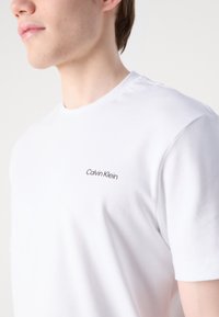 Fehér pamut póló, kerek nyakkivágással és rövid ujjakkal, fekete "Calvin Klein" logóval hímezve a mellkason.