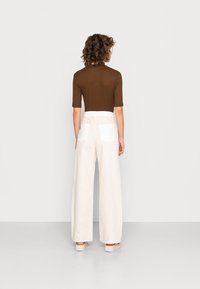 Top ajustado castanho com mangas três-quartos, combinado com calças largas de cintura alta em creme, com bolsos traseiros brancos.