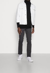 Vit denimjacka, svart rullkrage, grå byxor och vita sneakers. Klädseln har en avslappnad, lager-på-lager-look med kontrasterande färger.
