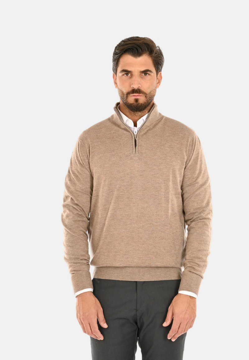 Maglione beige con zip, dalla texture morbida e maniche a costine, sovrapposto a una camicia bianca con colletto, abbinato a pantaloni grigi scuri.