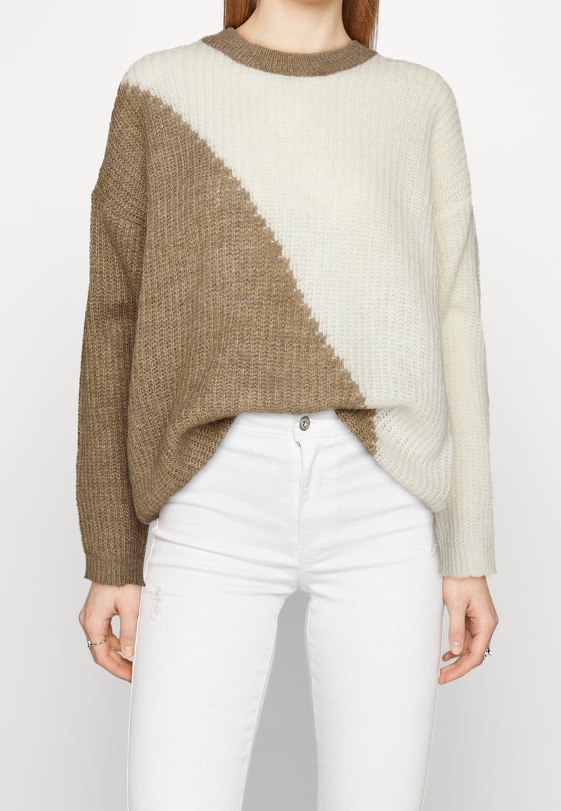 Paksu neulepusero, jossa on vinomustavalkoinen väriblokki, pyöreä pääntie ja pudotetut hartiat. Päälle puettuna valkoisten farkkujen kanssa.