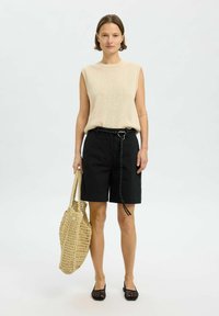 Pleteni brezrokavnik v bež barvi, črne kratke hlače z detajlom pasu, pletena torba v bež barvi in črne mrežaste balerinke. Minimalističen dizajn, vsakdanji videz.