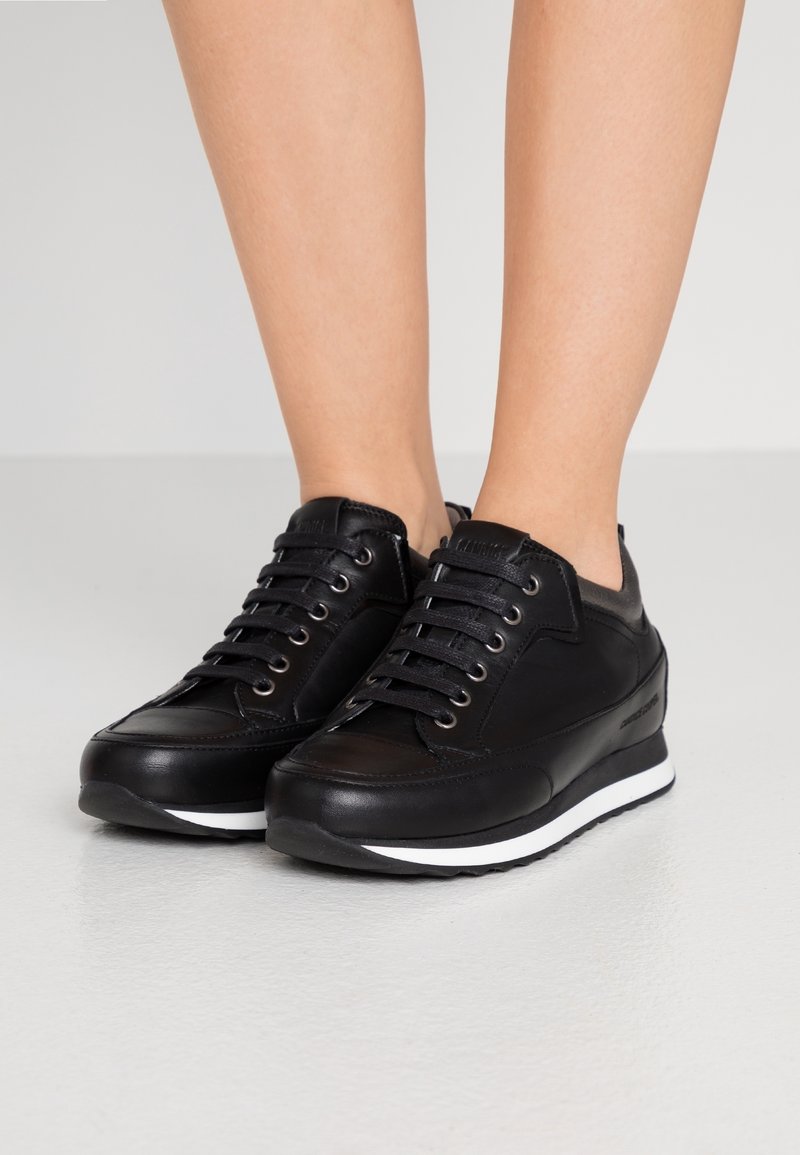 Svarta lädersneakers med rundad tå, snörning framtill och silverfärgade öglor. Har en vit mellansula och en strukturerad yta.