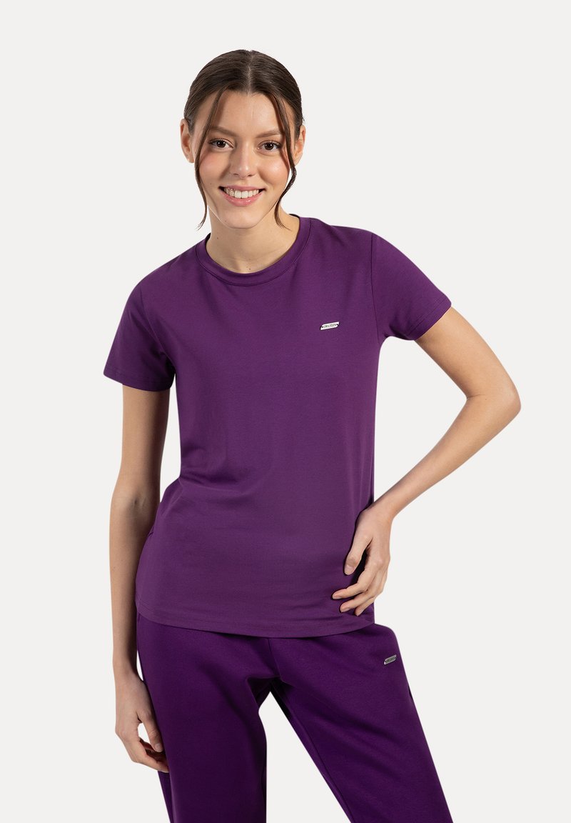 Camiseta morada hecha de algodón suave, con cuello redondo y mangas cortas. Detalle de pequeño logo en el lado izquierdo del pecho. Combinada con pantalones a juego.