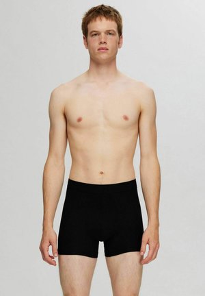 Schwarze Boxershorts mit glatter Textur, elastischem Bund und taillierter Passform, getragen von einem Modell mit freiem Oberkörper.