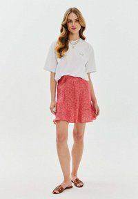 Bílá košile s krátkým rukávem a zeleným detailem, spárovaná s růžovou květinovou sukní. Sukně má rozšířený střih a je nošena s hnědými plochými sandály.