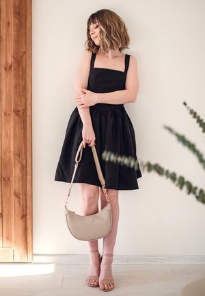 Schwarzes ärmelloses Kleid mit tailliertem Oberteil und weit ausgestellt Rock. Beiges Handtasche mit geschwungener Form und goldenen Beschlägen. Strumpfsandalen in Nude.