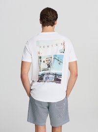Maglietta bianca a maniche corte con una stampa grafica colorata sul retro che raffigura immagini di Venezia, inclusi cartelli e palme.