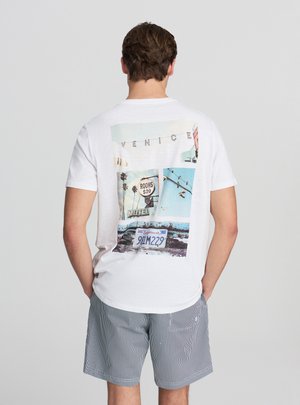 Maglietta bianca a maniche corte con una stampa grafica colorata sul retro che raffigura immagini di Venezia, inclusi cartelli e palme.