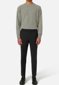 Maglione grigio a maglia, pantaloni neri slim e sneakers nere. Il maglione ha un collo rotondo; i pantaloni presentano pince davanti e una chiusura con bottone.