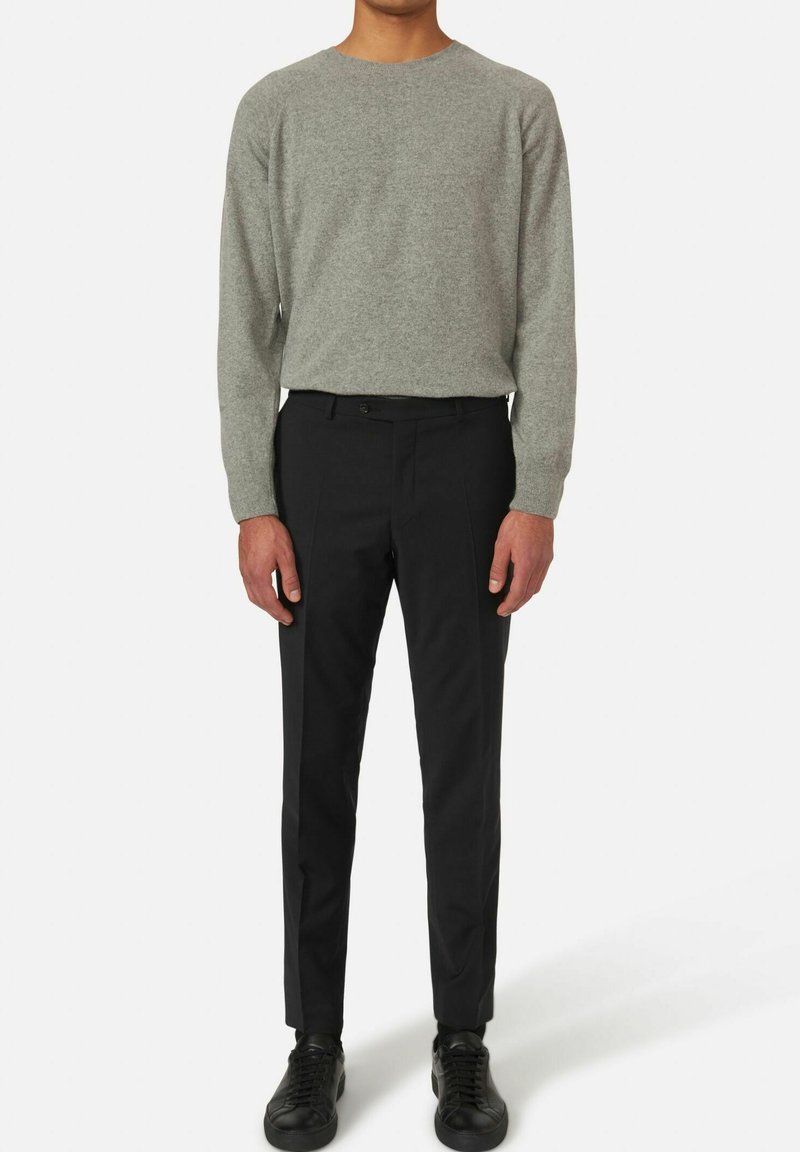 Maglione grigio a maglia, pantaloni neri slim e sneakers nere. Il maglione ha un collo rotondo; i pantaloni presentano pince davanti e una chiusura con bottone.