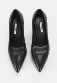 Schwarze Leder-Pumps mit hohen Absätzen und spitzer Zehenform, glatter Textur und gepolsterter Innensohle. Im Schuh mit "DESA" beschriftet.