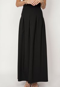 Czarna spódnica do ziemi wykonana z lekkiego materiału. Posiada fałdy w talii i gładką strukturę. Ma dopasowaną talię i brak widocznych wzorów.