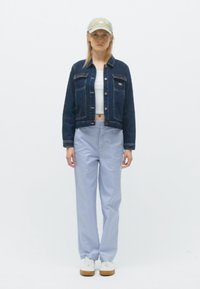 Traper jakna, bijeli crop top, svijetloplave hlače i bijele tenisice. Khaki kapa; minimalistički dizajn s osnovnim hardverom i bez uzoraka.