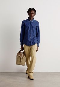 Marine knoop-overhemd, beige broek en bijpassende tas. Het overhemd heeft een kraag en de tas heeft een rits. Soepele texturen, eenvoudig ontwerp.