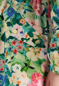 Bloemmotief stof in levendige kleuren met roze, blauwe en groene tinten. Inclusief een merkknoop in goud en een zachte textuur.