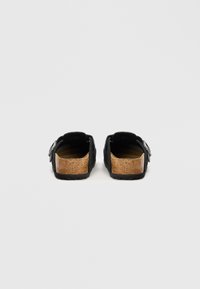 Fekete, csúsztatható szandálpár, parafa talppal és állítható oldalszíjakkal, hátulról nézve, sima fehér háttér előtt.