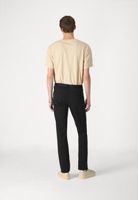 T-shirt en coton beige et pantalon slim noir portés avec des chaussures beiges. Le t-shirt a un col rond et le pantalon possède des poches arrière.