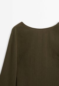 Vêtement vert olive foncé à manches longues avec un large col arrondi, montré depuis la partie supérieure du dos sur un fond blanc.