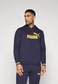 Felpa blu navy realizzata in misto cotone, con un grande logo PUMA giallo, cappuccio con cordino e polsini a costine con strisce gialle.