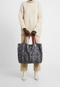 Grote zwart-wit slangenprint schoudertas met dubbele rode en marineblauwe gestreepte handvatten, gemaakt van gestructureerde stof.