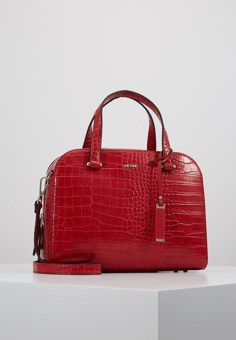 Sac à main rouge en cuir embossé crocodile avec doubles poignées, bandoulière amovible, fermeture éclair et logo métallique. Texture lisse et brillante.