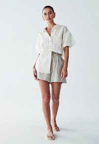 Linnen shirt met korte mouwen in gebroken wit met knopen, gecombineerd met lichtgrijze shorts met trekkoord. Heeft een relaxte pasvorm en een zachte textuur.