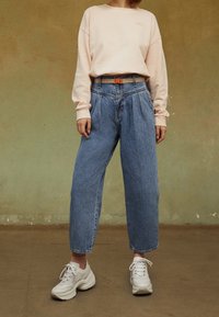 Vaaleanpunainen huppari, vaaleansiniset korkeavyötäröiset housut, joissa on laskokset, ja valkoiset lenkkarit. Yksivärisiä, joissa on minimaalista yksityiskohtaa, rento leikkaus.