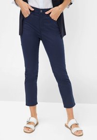 Marineblauwe katoenmixbroek met een slim fit, cropped lengte, voorzakken en een metalen knoopsluiting. Gecombineerd met witte sandalen.