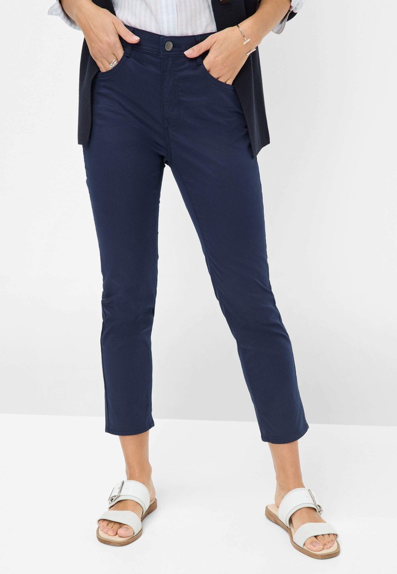 Marineblauwe katoenmixbroek met een slim fit, cropped lengte, voorzakken en een metalen knoopsluiting. Gecombineerd met witte sandalen.