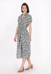 Rochie florală alb-negru, cu guler, mâneci scurte răsucite, talie elastică și tiv de lungime medie. Asortată cu tocuri cu bloc de culoare bej.