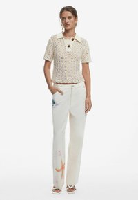 Pletený top s krémovým golierom a veľkým gombíkom; skombinovaný s bielymi nohavicami s farebnou vyšívanou námornou tematikou.