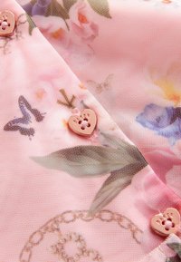 Ziedu raksts audumā rozā krāsā ar zaļiem un ziliem akcentiem, ar sirds formas pogu, kurai ir pēdas dizains. Gaisīgs, teksturēts materiāls.