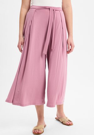 Helle rosa weite Stoffhosen mit einem Bindegürtel, verziert mit Falten und einem lässigen Schnitt. Kombiniert mit neutralen Sandalen.