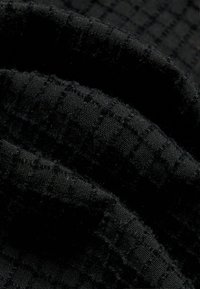 Detailný pohľad na zloženú čiernu látku s textúrovaným, mriežkovým vzorom a jemnými, chlpovými povrchovými detailmi.