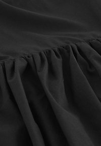 Tissu noir présentant des sections froncées, une texture lisse et un léger éclat, mettant en valeur des drapés doux et des éléments de design fluides.