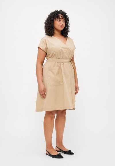 Beige wrap-mekko, jossa on V-pääntie, lyhyet hihat, vyö vyötäröllä ja kaksi sivutaskua. Yhdistetty mustiin avokkaisiin.