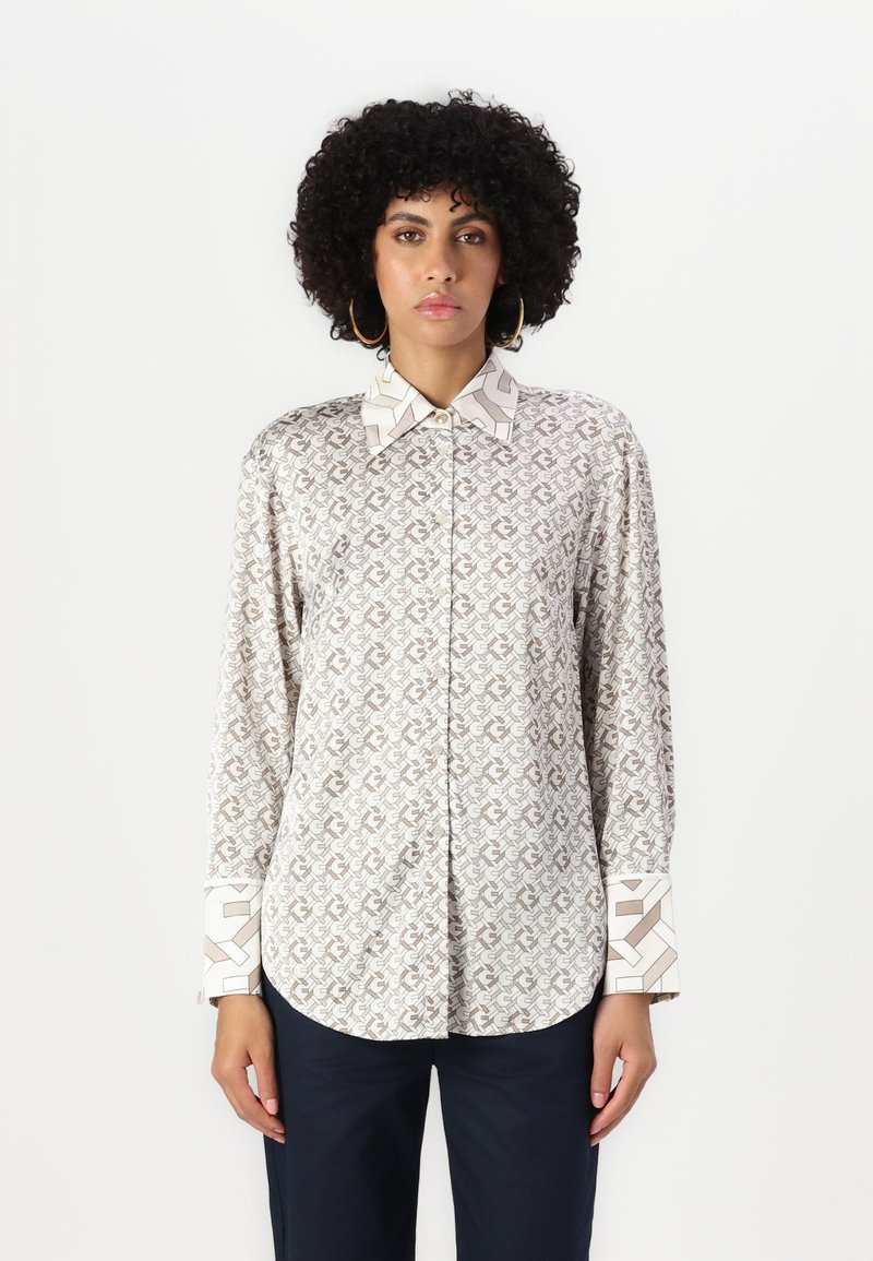Long-sleeve shirt in a light beige fabric featuring a repeated brown abstract pattern, contrasting patterned cuffs and collar edges.