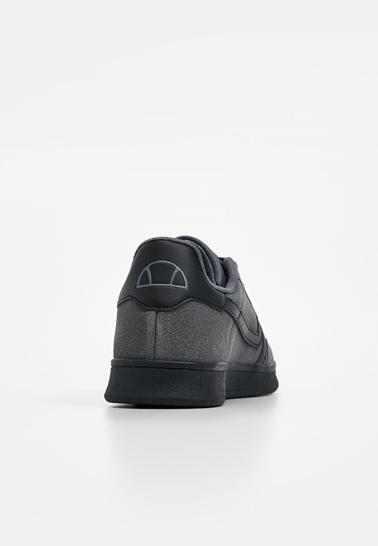 Zapatilla negra con un upper de ante suave, talón redondeado y un logo sutil en la parte trasera. Presenta paneles laterales texturizados y una suela de goma plana.