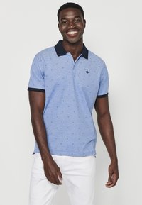 Kortärmad polo-skjorta i ljusblått med marinblå krage, med en subtil mönstrad design och ett litet emblem på vänster bröst.