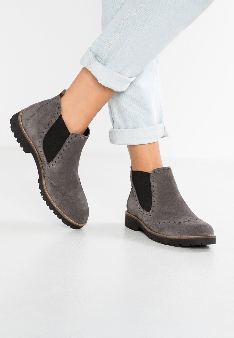 Grå mockakängor med svarta elastiska sidopaneler, brogue-detaljer och en strukturerad gummisula för bra grepp.