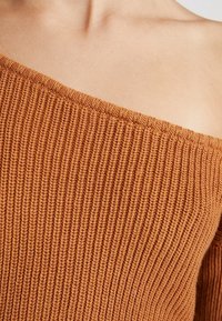 Off-Shoulder-Ripp-Strickpullover aus verbranntem Orange, mit weitem Ausschnitt und strukturiertem Muster.