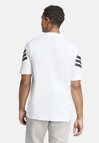 Camiseta de algodón blanca con rayas negras en los hombros, mangas cortas y cuello redondeado. El diseño es simple y clásico.