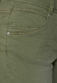 Denim vert olive à la texture lisse, doté d'une poche arrière, de boutons argentés et de surpiqûres visibles sur les côtés.