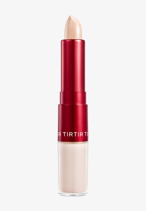 Producto labial con una barra cremosa de color beige en la parte superior de un mecanismo giratorio metálico rojo, alojado en una base cilíndrica transparente.