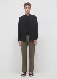 Chemise noire à boutons avec col mandarin, pantalon vert olive, et sandales noires. Le tissu paraît lisse, avec une coupe décontractée.