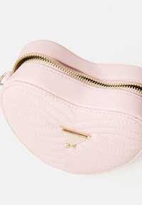 Borsa a forma di cuore rosa realizzata in pelle sintetica trapuntata, con una cerniera dorata e un emblema triangolare dorato del marchio.