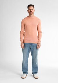 Helles rosa langärmliges Sweatshirt mit rundem Ausschnitt, kombiniert mit hellblauen Jeans und weißen Sneakers mit braunen Sohlen. Einfaches Design.
