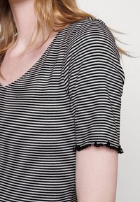 Black and white striped short-sleeve top with a V-neck and lace-trimmed hem. The fabric appears soft with a smooth texture.